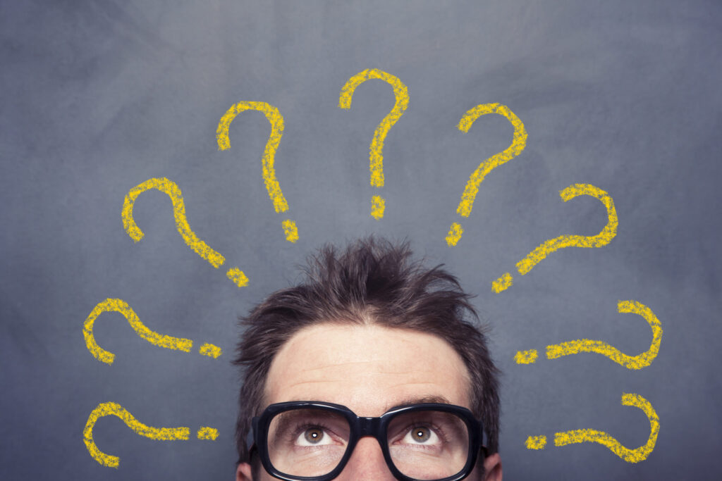 A photo of a man's face and head. His hair is messy; his glasses are large, round, and black. Chalk-style question marks, nine in total, surround his head like a halo of confusion.