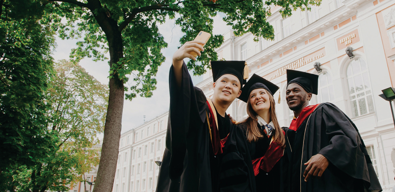 Three graduates posing for a selfie one of them is taking of the group.